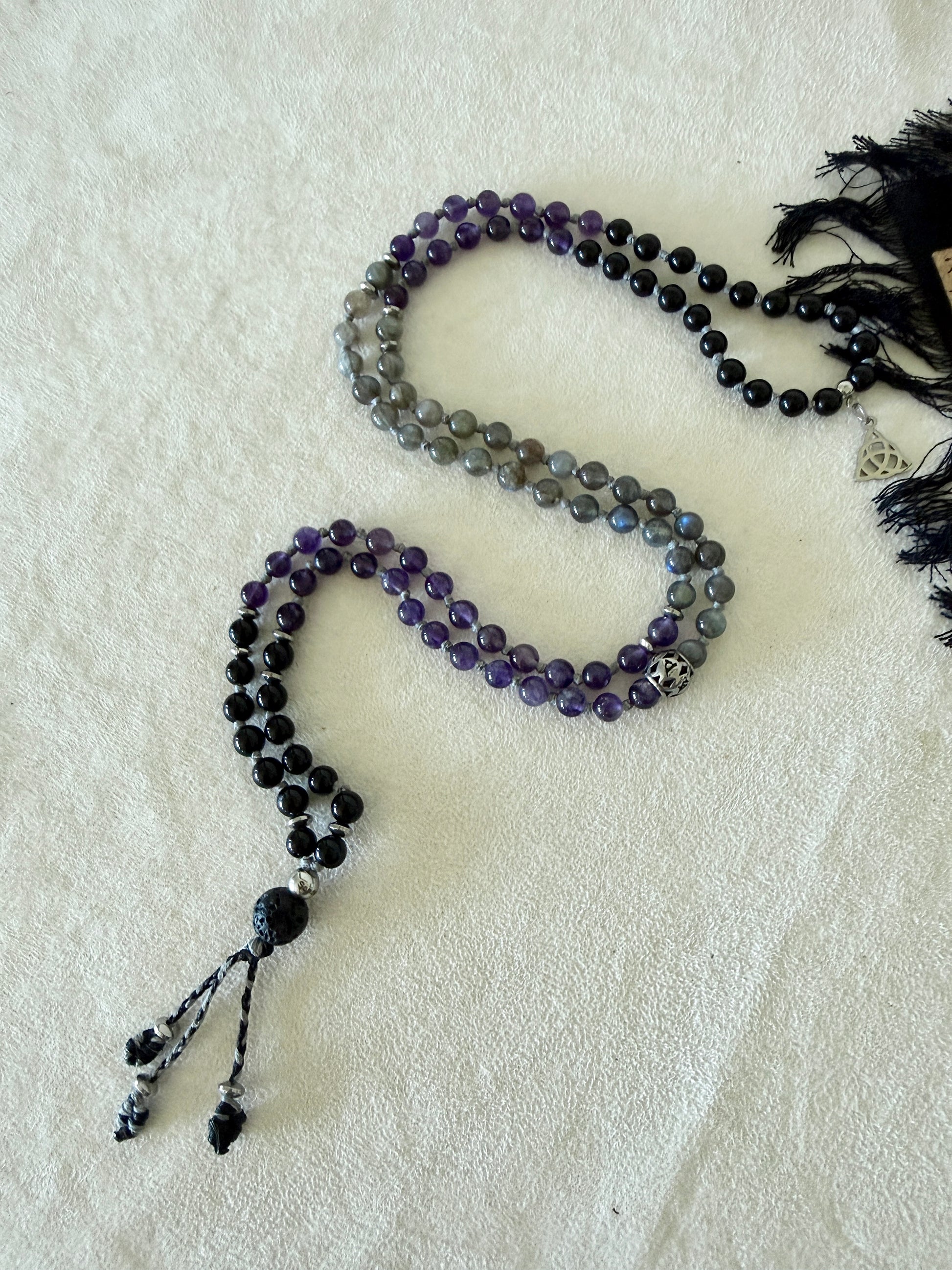 Shadow Work Mini Mala coiled to show the full 6mm bead pattern in obsidian, amethyst, and labradorite, with Triquetra charm and lava stone meru.