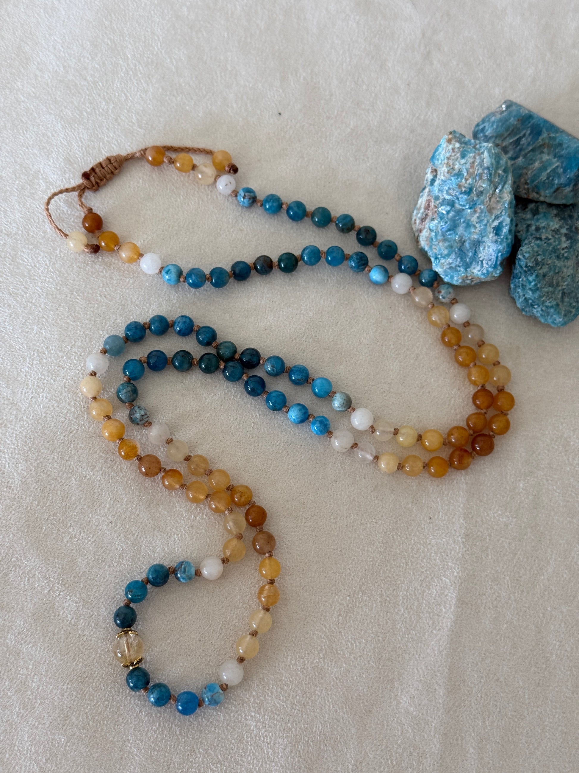 full view of The Sun and the sea natural gemstone mala bracelet. Handmade Apatite and Yellow Jade mala bracelet with natural 6 mm gemstones, Citrine guru bead, adjustable macramé closure, and stainless steel details; a 108 bead mala necklace inspired by sea and sun, water and fire, for meditation, yoga, and intention practice.