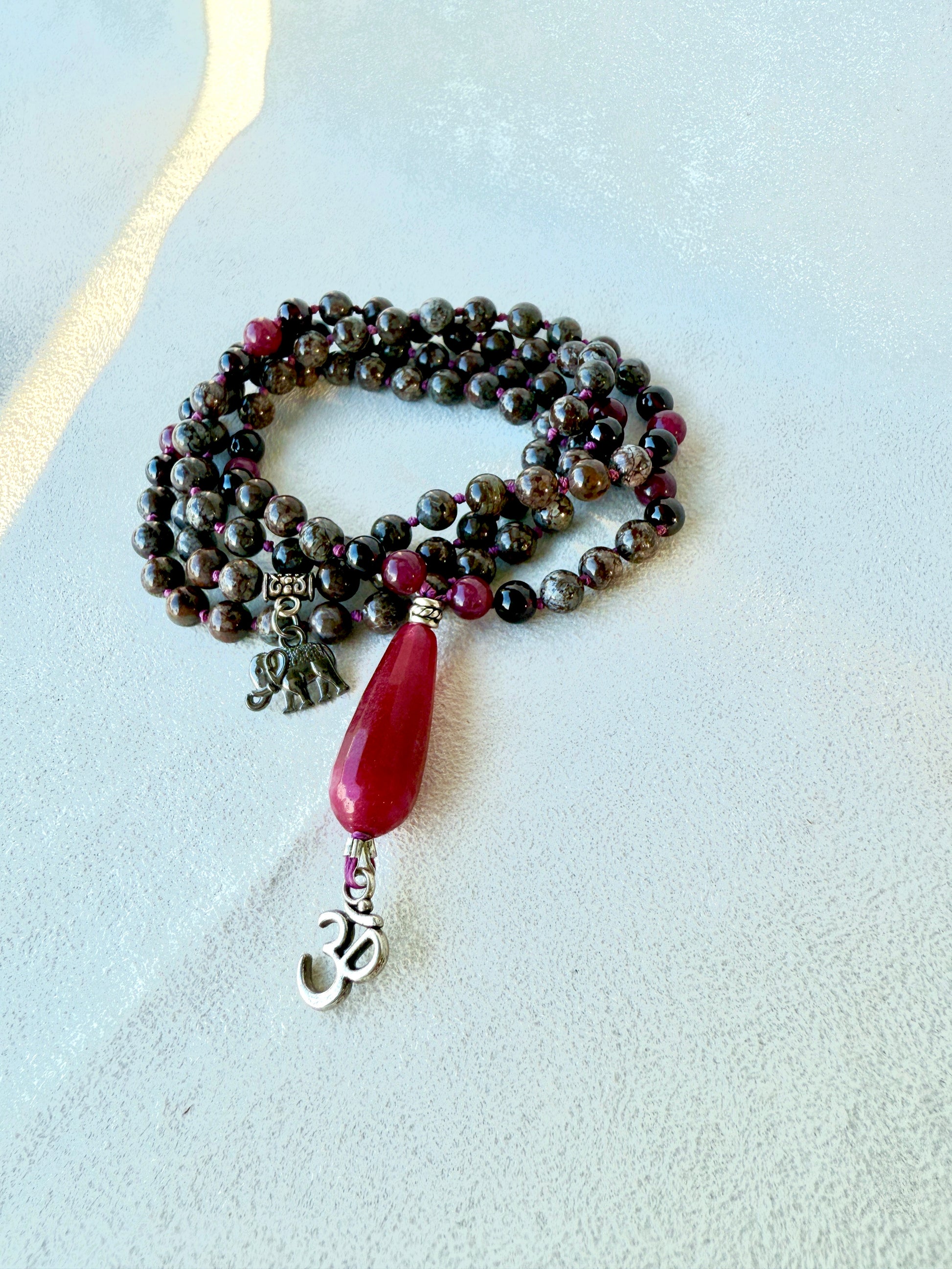 Detail of guru bead and tassel on snowflake obsidian garnet mala necklace and om pendant