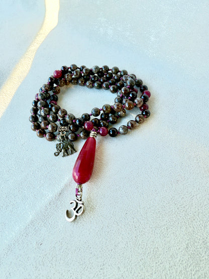 Detail of guru bead and tassel on snowflake obsidian garnet mala necklace and om pendant