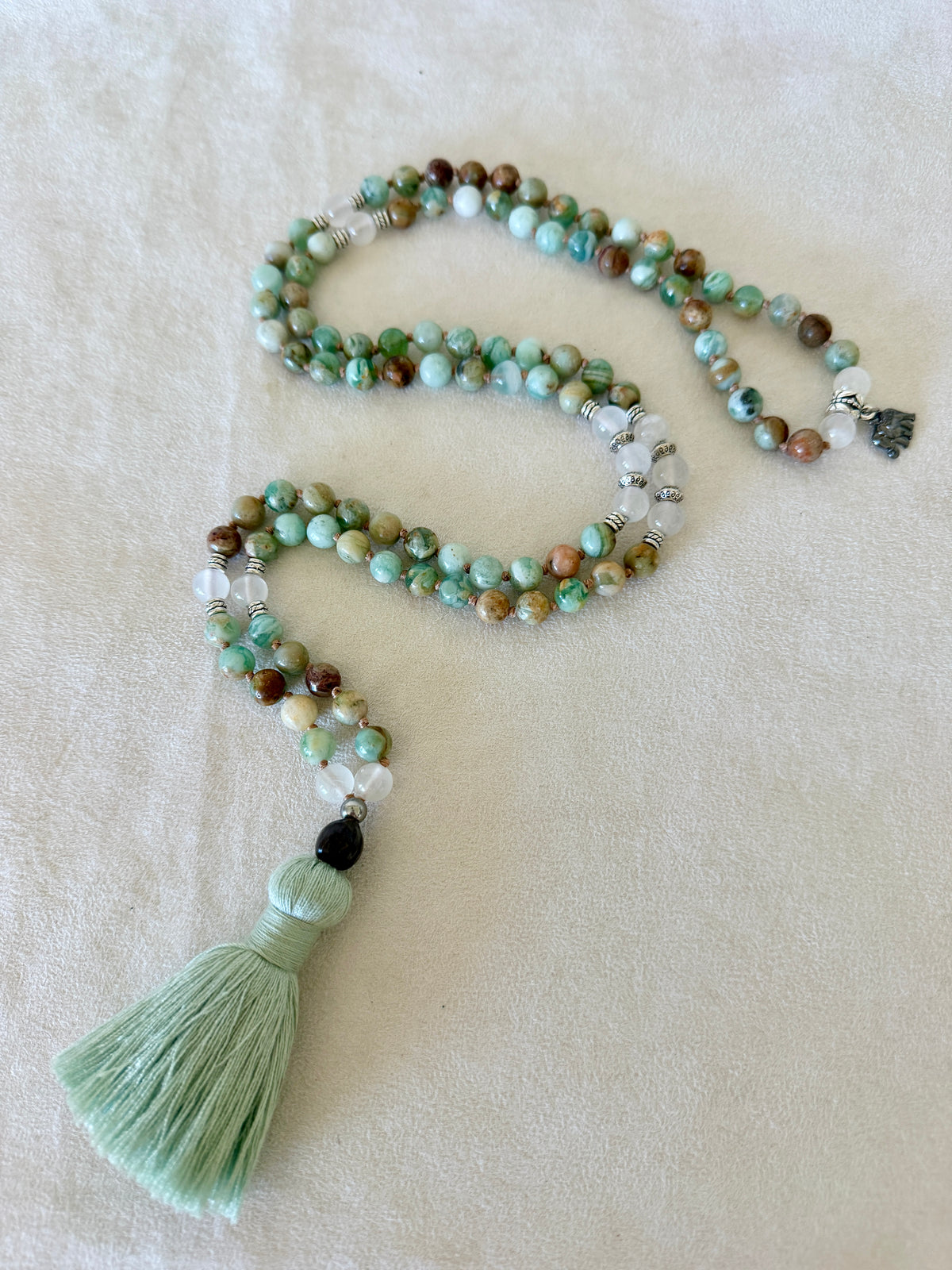 Full-length green quartz and selenite mala laid out from elephant charm to cotton tassel