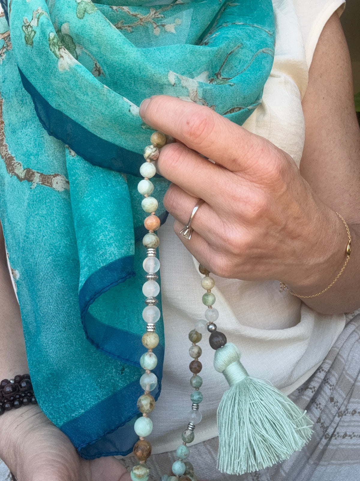 Close-up of a woman's hand touching the green quartz and selenite mala beads and cotton tassel