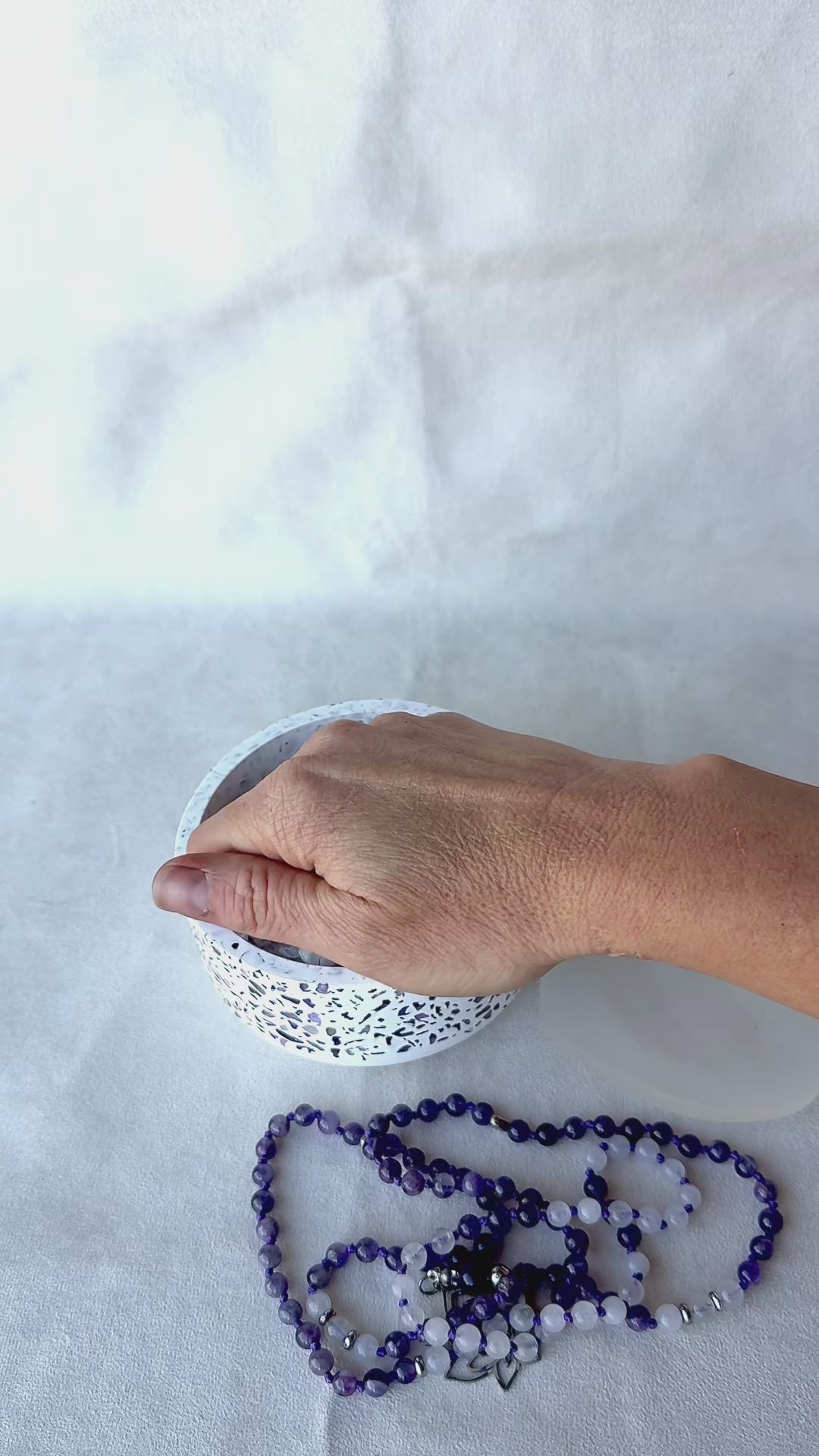 Close-up of Video featuring a bowl with natural clear quartz and amethyst crystals for energy cleansing of mala beads