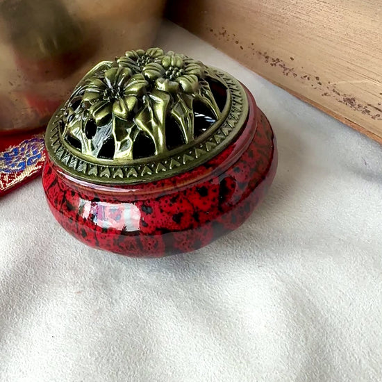 video of Small round ceramic bowl in deep red glaze with a removable golden metallic lid, artisanal tabletop decor.