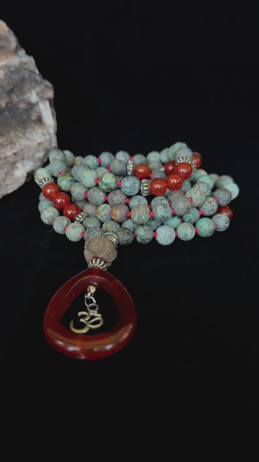Video of 108 mala necklace with grounding spiritual jewelry with turquoise and red gemstone beads. Handmade in US mala for meditation and intention setting.