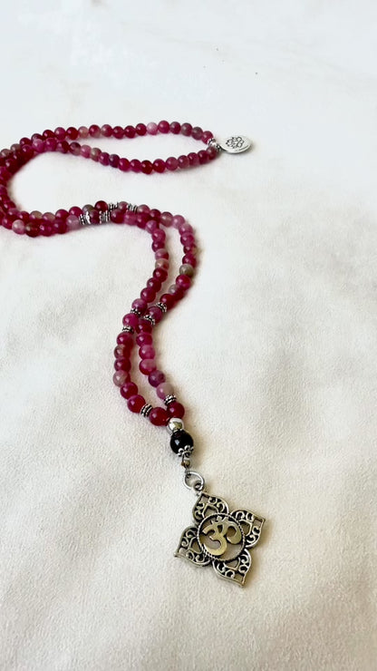 Video preview of Mala necklace in watermelon tourmaline for heart chakra healing. Heart chakra mala beads necklace with OM and lotus charm. Mala for Meditation for women with watermelon tourmaline and garnet for heart protection and clarity with Anahata chakra pendant.