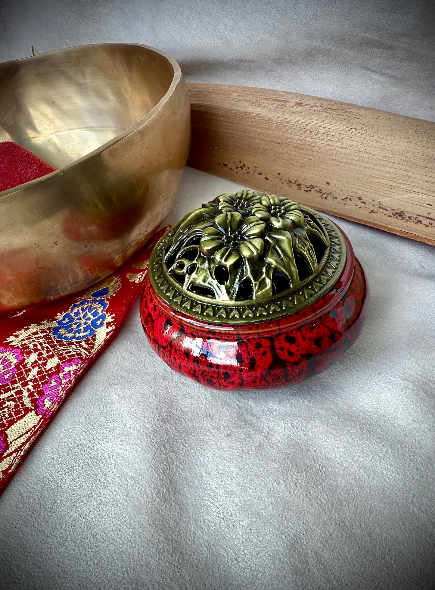 Small round ceramic bowl in deep red glaze with a removable golden metallic lid, artisanal tabletop decor.