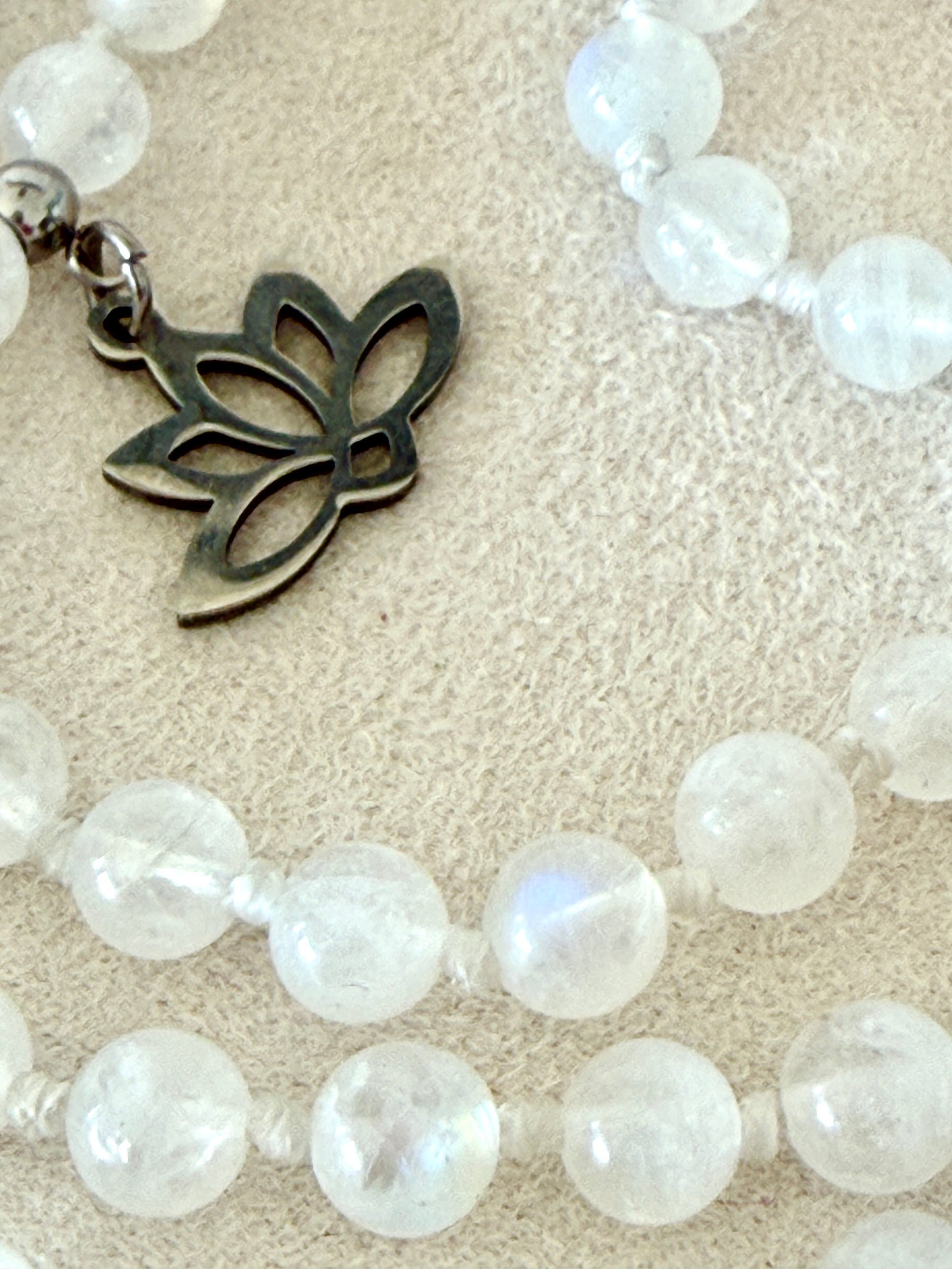 small lotus charm, detail on a Hand-knotted Rainbow Moonstone mala necklace with 108 prayer beads, 6 mm natural gemstone beads, Aqua Aura Quartz meru, stainless steel details.