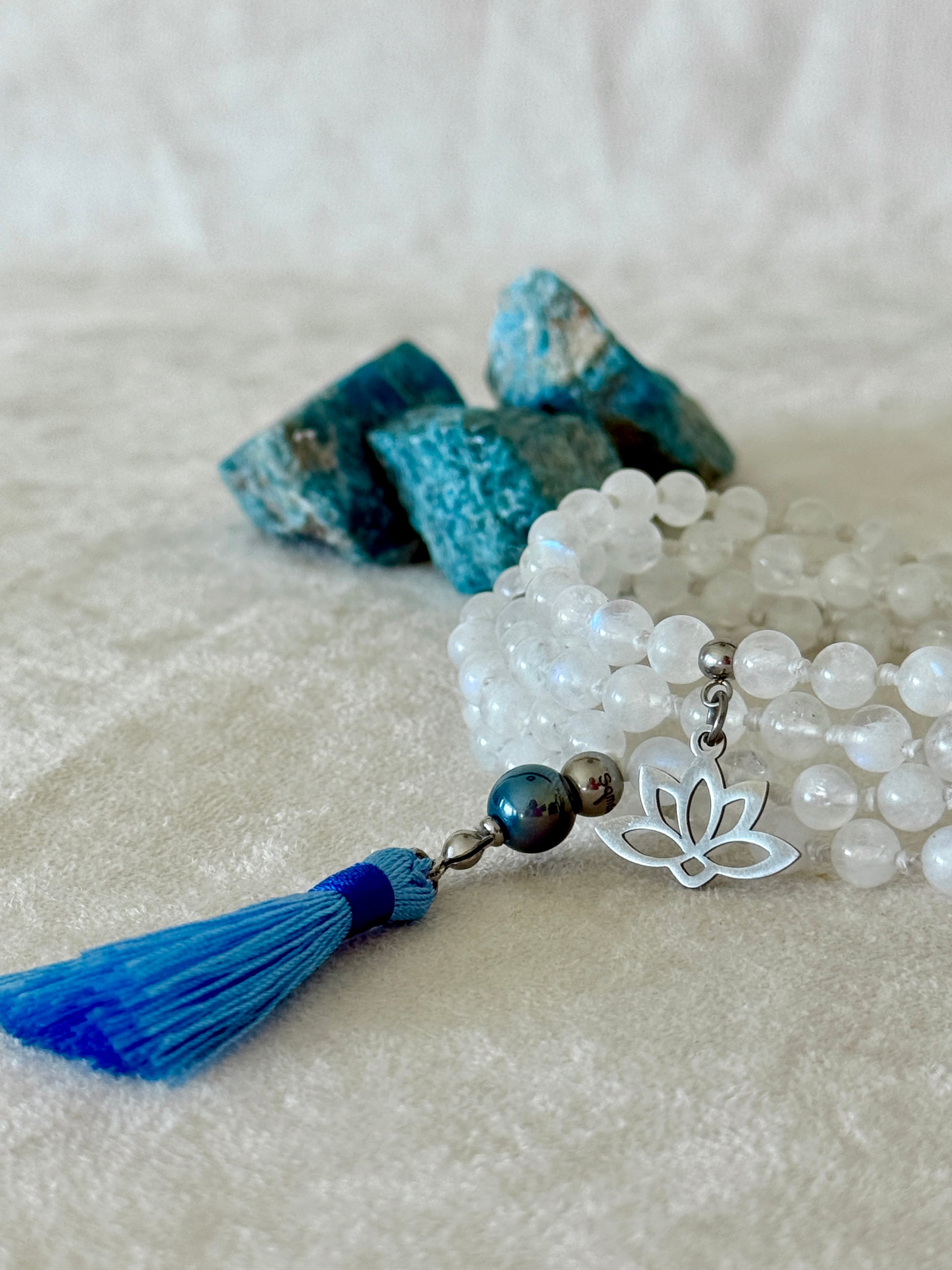 Handmade Rainbow Moonstone mala for meditation with 108 prayer beads, 6 mm natural gemstone beads, Aqua Aura Quartz meru, stainless steel details, small lotus charm, and tassel, created for meditation, breathwork, mantra repetition, mindfulness, and intentional practice. Samdea Mala