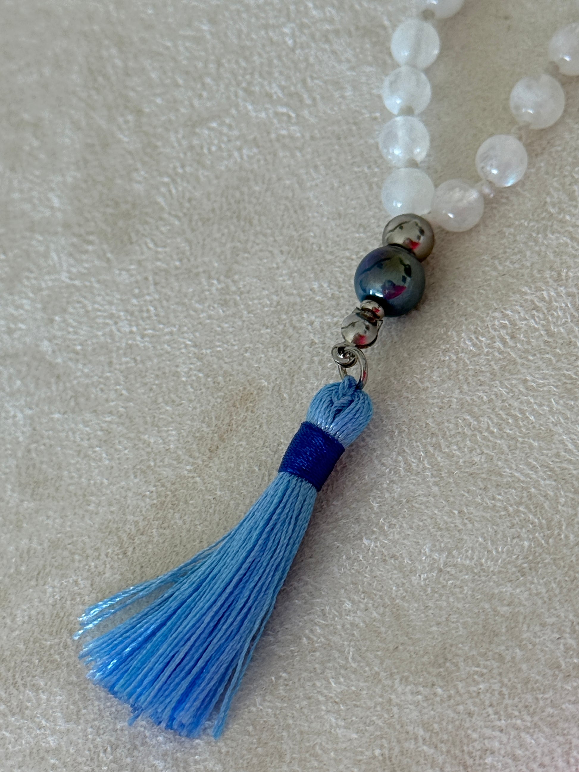 tassel detail on a Handmade Rainbow Moonstone mala for meditation with 108 prayer beads, 6 mm natural gemstone beads, Aqua Aura Quartz meru, stainless steel details.