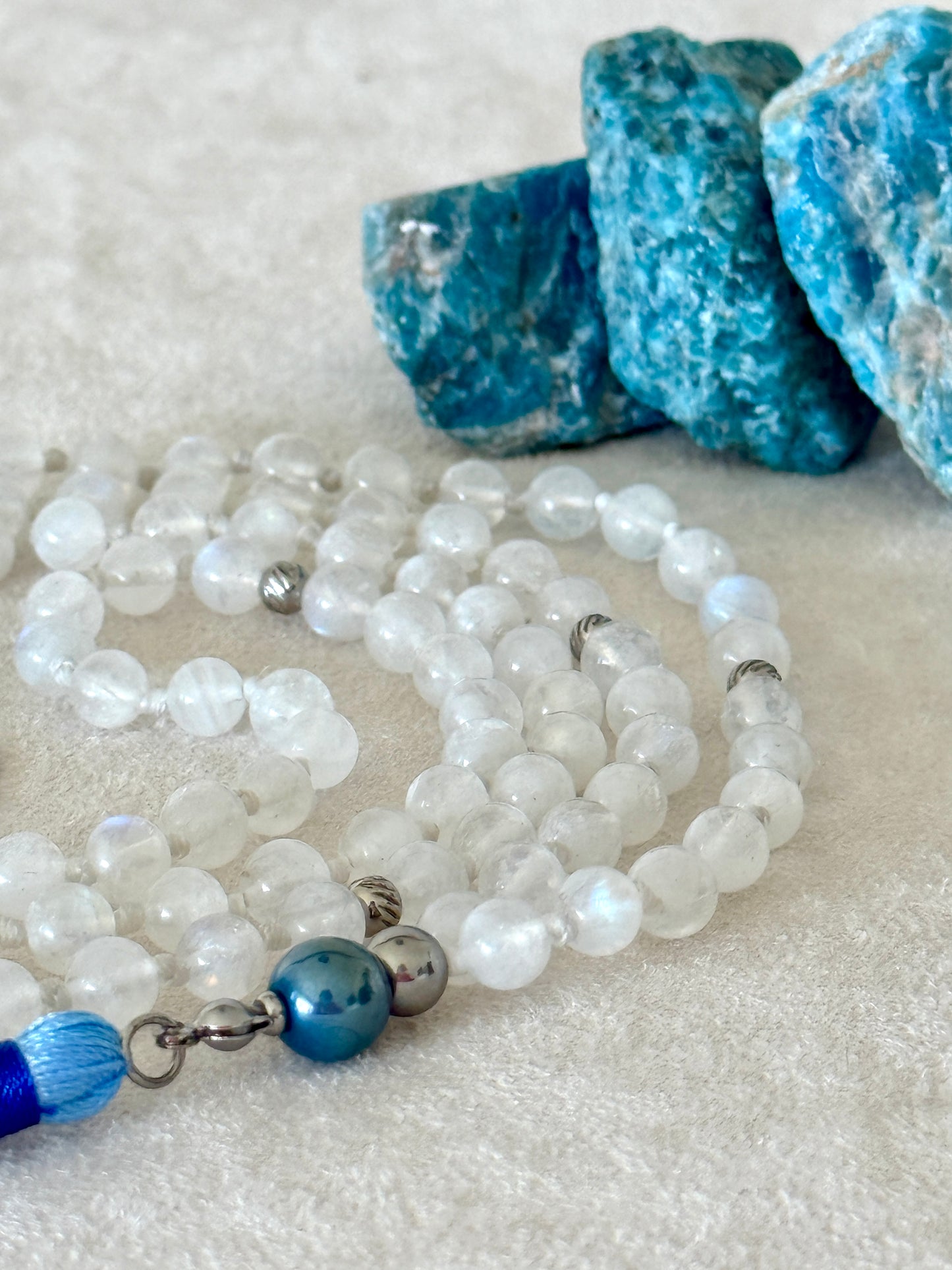 Handmade Rainbow Moonstone mala for meditation with 108 prayer beads, 6 mm natural gemstone beads, Aqua Aura Quartz meru, stainless steel details, small lotus charm, and tassel, created for meditation, breathwork, mantra repetition, mindfulness, and intentional practice. Samdea Mala